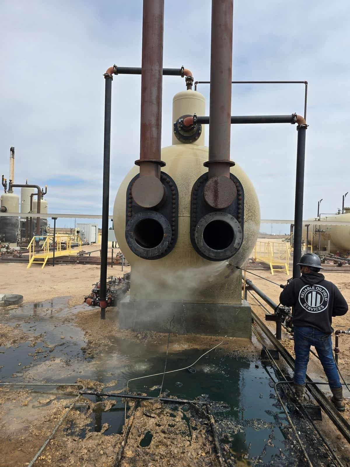 An ROS technician washing down a heater treater during a fired-equipment service call