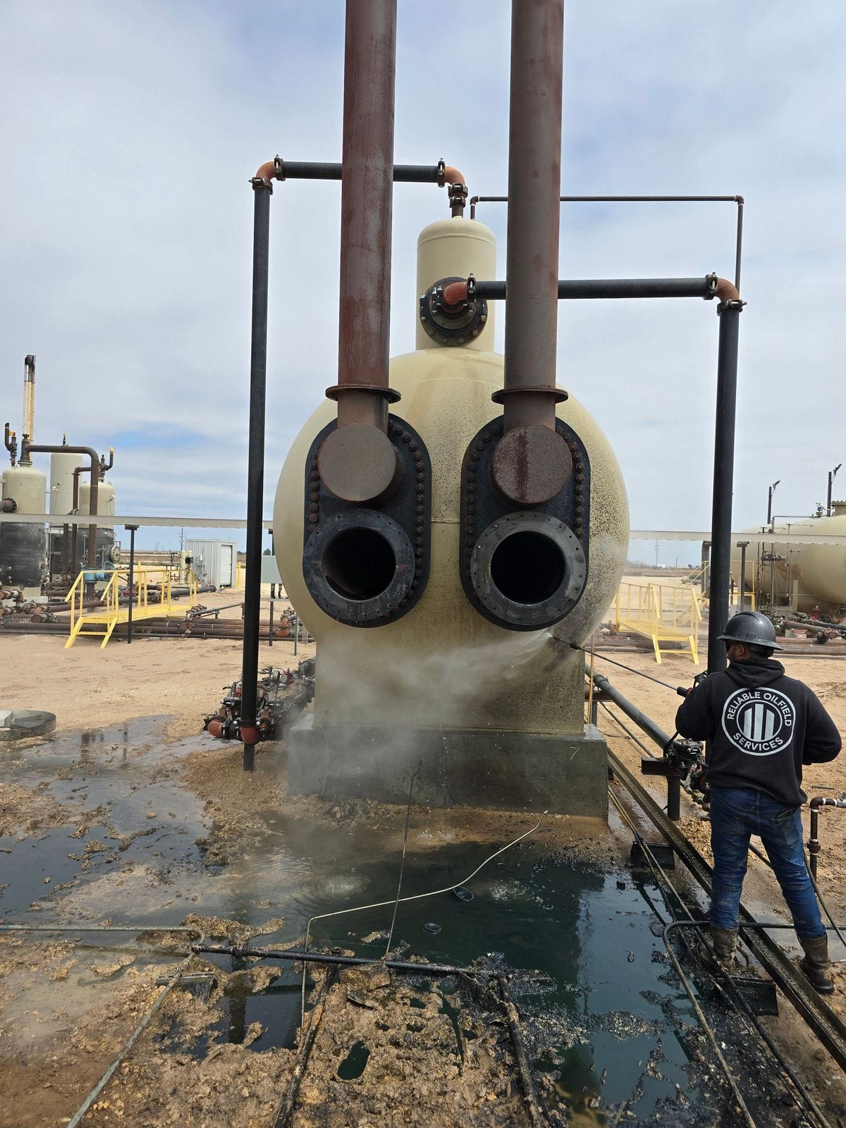 An ROS technician washing down a heater treater on a Permian Basin tank battery